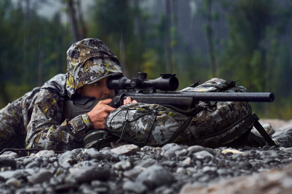 Detalle de cazador con equipo en lluvia junto a rifle Blaser R8 Professional 2.0