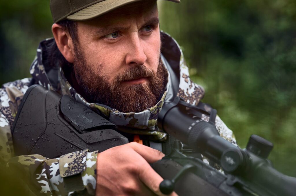 Primer plano de cazador con Blaser R8 Professional 2.0 en entorno de bosque y lluvia