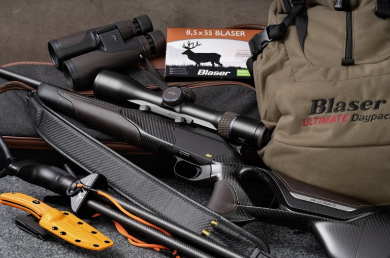 Rifle Blaser R8 Ultimate Carbon con visor, mochila Blaser y munición 8,5x55 sobre equipo de caza.