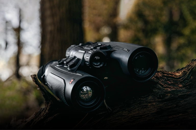 Binocular HIKMICRO HABROK 4K 2.0 apoyado sobre un tronco en el bosque